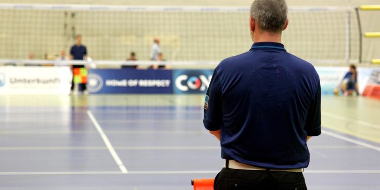 Kapalı salonda voleybol sahasına arkası dönük duran hakem.
