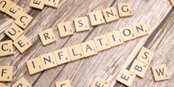 Ahşap Scrabble harfleriyle oluşturulmuş 'Rising Inflation' yazısı ve etraftaki harfler.