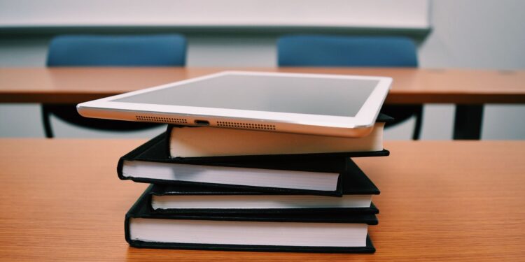 Ahşap masa üzerinde duran kitaplar ve üstünde dijital tablet.