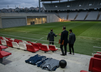 Futbol sahasındaki tribünlerde duran yetkililer planlama yapıyor.
