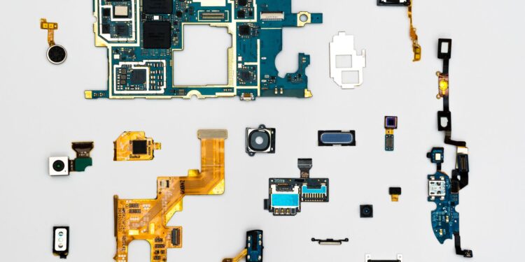 Sökülmüş akıllı telefon parçaları ve elektronik devre kartları düz zeminde sergileniyor.