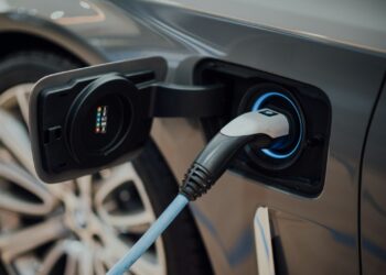 Gri renkli elektrikli bir otomobilin şarj istasyonuna bağlanmış şarj soketi.