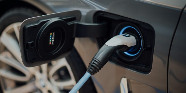 Gri renkli elektrikli bir otomobilin şarj istasyonuna bağlanmış şarj soketi.