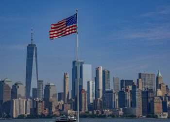 New York silüeti önünde dalgalanan Amerikan bayrağı ve denizdeki feribot.