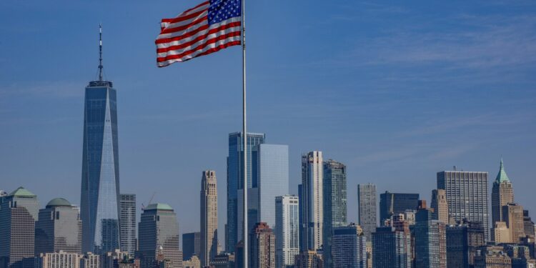 New York silüeti önünde dalgalanan Amerikan bayrağı ve denizdeki feribot.