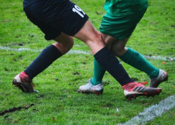 Çamurlu sahada mücadele eden futbolcuların bacaklarının ve kramponlarının yakın plan görüntüsü.
