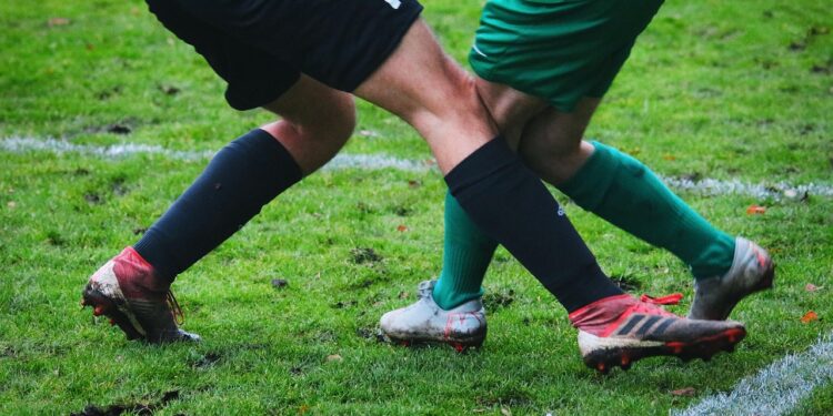 Çamurlu sahada mücadele eden futbolcuların bacaklarının ve kramponlarının yakın plan görüntüsü.