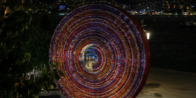 Gece vakti İstanbul silüeti önünde renkli ışıklı dairesel sanat enstalasyonu.