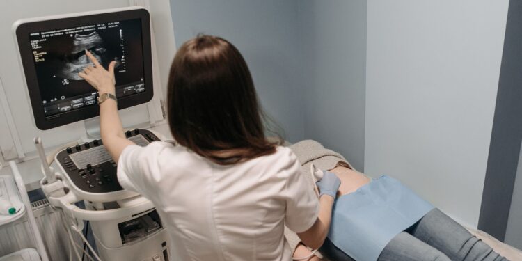 Doktor hastaya ultrason cihazı ile inceleme yapıyor ve ekrandakileri gösteriyor.