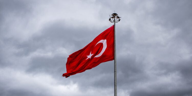 Bulutlu gökyüzü altında dalgalanan büyük Türk bayrağı ve aydınlatma direği.