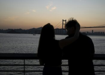 Gün batımında köprü önünde kucaklaşan romantik bir çift silüeti.