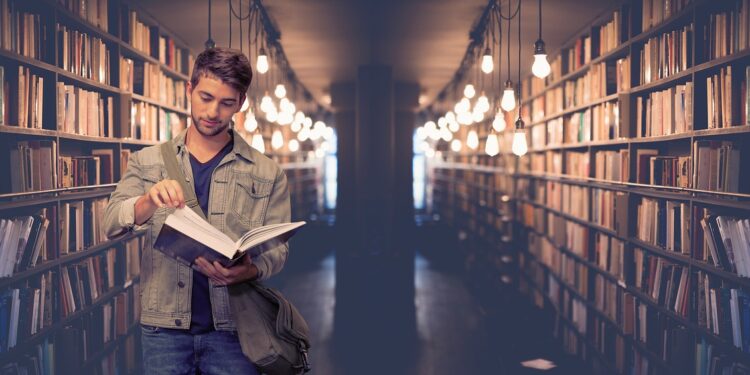 Kütüphanede kitap rafları arasında kitap inceleyen genç bir öğrenci.
