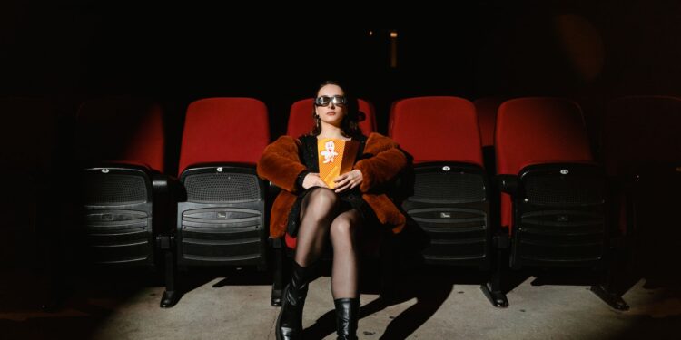 Sinema salonunda kırmızı koltukta oturup patlamış mısır yiyen kadın