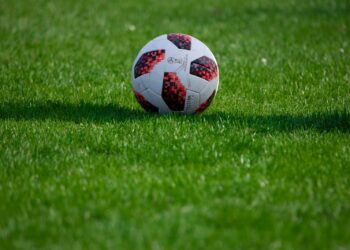 Çim saha üzerinde duran kırmızı ve beyaz desenli futbol topu.