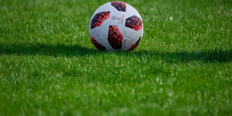 Çim saha üzerinde duran kırmızı ve beyaz desenli futbol topu.