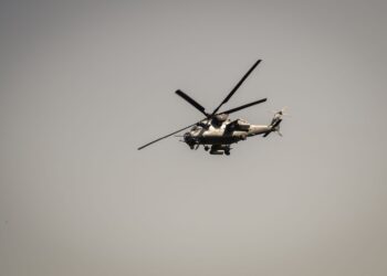 Gri askeri helikopter gökyüzünde tek başına uçarken havada süzülüyor.