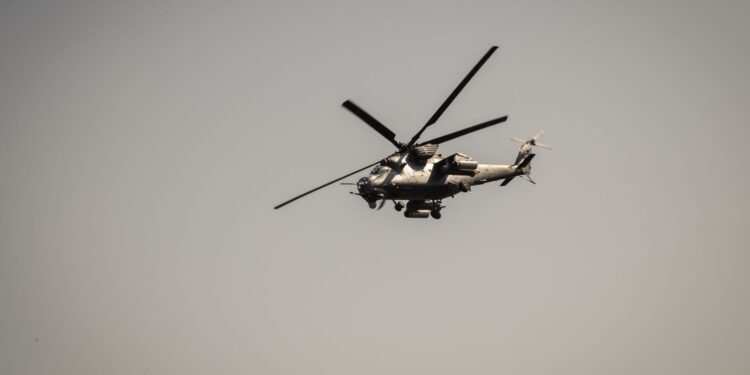 Gri askeri helikopter gökyüzünde tek başına uçarken havada süzülüyor.