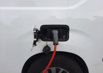 Beyaz renkli bir elektrikli araca şarj kablosu takıldığı anın yandan çekimi.