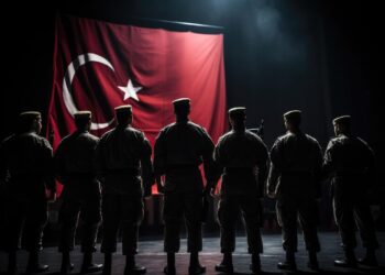 Türkiye bayrağının önünde saygı duruşunda duran askerlerin arkadan görünümü.