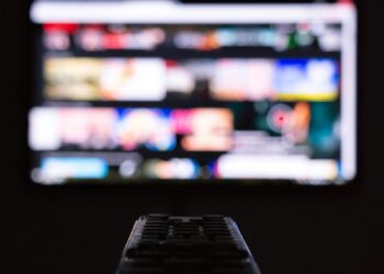 Karanlık odada televizyon izlerken elinde kumanda tutan bir kişi görünüyor.